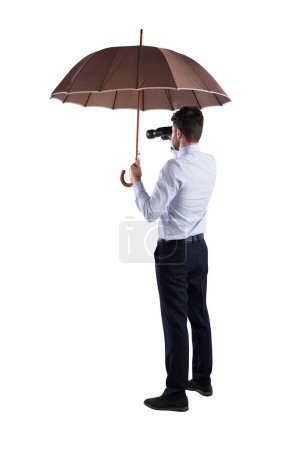 Foto de El hombre se cubre con un paraguas y mira lejos con un binocular - Imagen libre de derechos