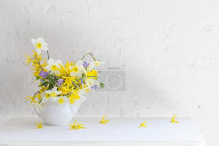Téléchargez les photos : Fleurs printanières blanches et jaunes en vase sur table en bois sur fond blanc - en image libre de droit