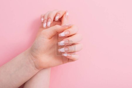 Foto de Manos femeninas con hermosas uñas largas con manicura con patrón de corazón sobre fondo rosa - Imagen libre de derechos