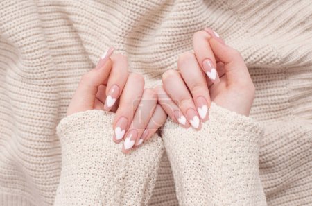 Foto de Manos femeninas con hermosas uñas largas con manicura con patrón de corazón en ropa de invierno - Imagen libre de derechos