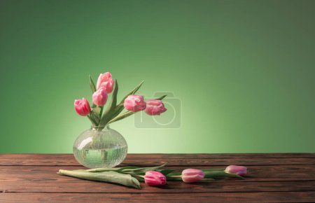 Photo for Pink tulips in glass vase on green background - Royalty Free Image