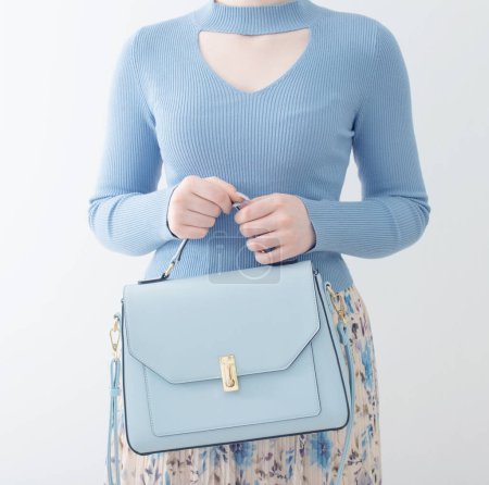 Téléchargez les photos : Jeune fille en chemisier bleu et jupe plissée avec sac à main bleu sur fond blanc - en image libre de droit