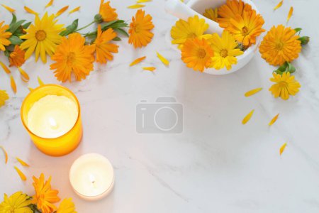Téléchargez les photos : Fleurs de souci orange avec des bougies allumées sur fond de marbre blanc - en image libre de droit