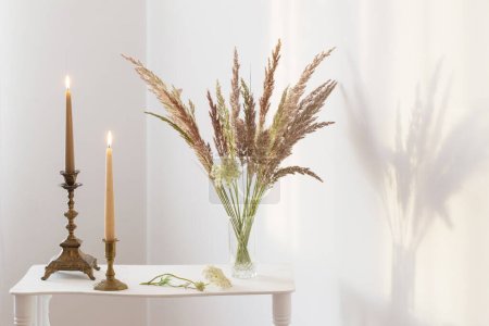 Téléchargez les photos : Bouquet de fleurs sauvages et de bougies brûlantes à la lumière du soleil à l'intérieur blanc - en image libre de droit