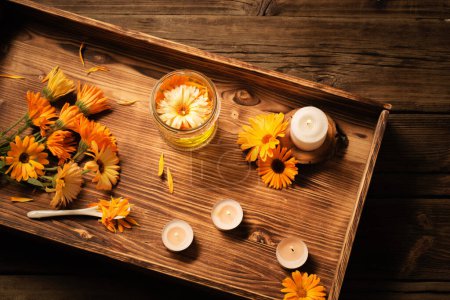 Téléchargez les photos : Fleurs médicinales de calendula et huile d'arôme avec des bougies allumées sur plateau sur fond de bois foncé - en image libre de droit