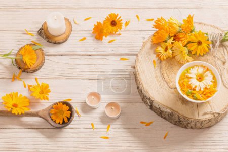 Téléchargez les photos : Fleurs médicinales de calendula avec des bougies allumées sur fond de bois blanc - en image libre de droit