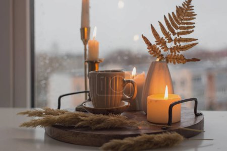 Téléchargez les photos : Nature morte d'automne avec des bougies allumées et une tasse de café sur le fond d'une fenêtre avec des gouttes de pluie - en image libre de droit