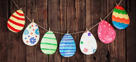 Foto de Papel huevos pintados de Pascua pintados cuelgan de pinzas de ropa en el fondo pared de madera vieja
. - Imagen libre de derechos