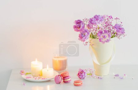 Téléchargez les photos : Bouquet de fleurs roses de printemps et de bougies allumées sur table blanche - en image libre de droit