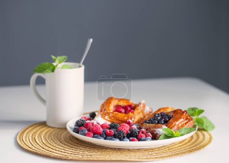 Foto de Danés con frambuesas y arándanos en plato redondo con bayas en mesa blanca - Imagen libre de derechos