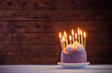 Téléchargez les photos : Gâteau d'anniversaire violet avec des bougies allumées sur fond de bois foncé - en image libre de droit