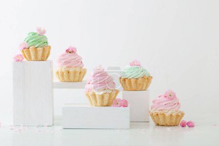 Photo for Pink and green cupcakes with spring flowers  on wooden podiums on white  background - Royalty Free Image