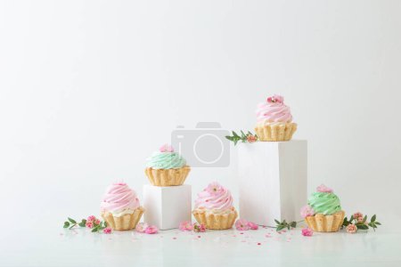 Foto de Cupcakes rosas y verdes con flores de primavera sobre podios de madera sobre fondo blanco - Imagen libre de derechos