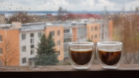 café en verre thermique sur fond fenêtre avec gouttes de pluie