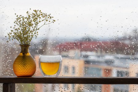 Téléchargez les photos : Thé chaud en verre thermique sur la fenêtre de fond avec des gouttes de pluie - en image libre de droit