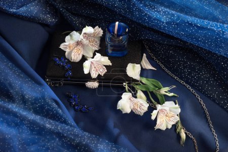 Foto de Botella de perfume, embrague negro y joyas en el fondo de vestido de noche azul - Imagen libre de derechos