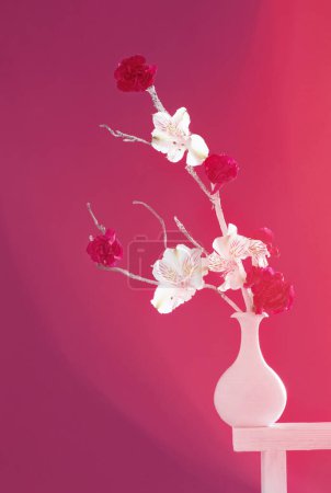 Foto de Inusual ramo en jarrón blanco en estante blanco sobre fondo rosa - Imagen libre de derechos