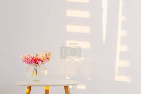 Téléchargez les photos : Fleurs de printemps dans un vase en verre sur fond blanc mur en plein soleil - en image libre de droit