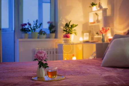 Foto de Acogedor dormitorio por la noche con flores y té - Imagen libre de derechos