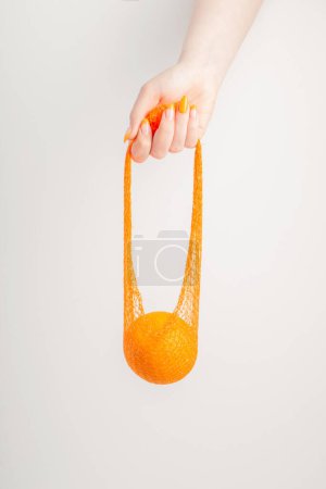 Téléchargez les photos : Main féminine avec sac à ficelle orange et synthétique - en image libre de droit