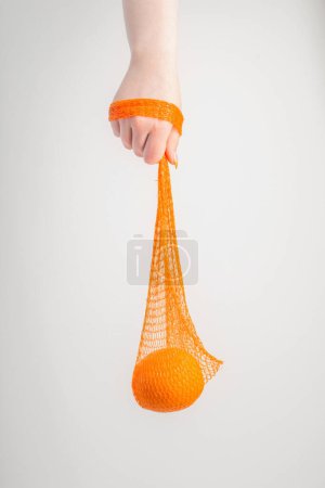Photo for Female hand with orange and synthetic string bag - Royalty Free Image