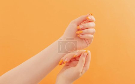 Foto de Mano femenina con manicura sobre fondo naranja - Imagen libre de derechos