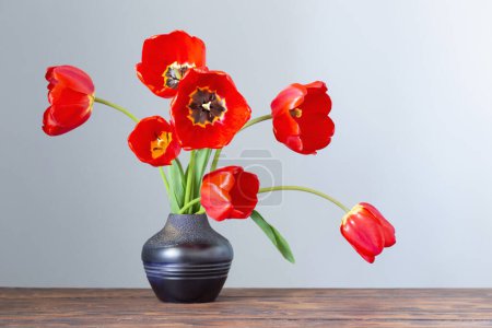 Foto de Tulipanes rojos en jarrón de cerámica oscura sobre mesa de madera - Imagen libre de derechos