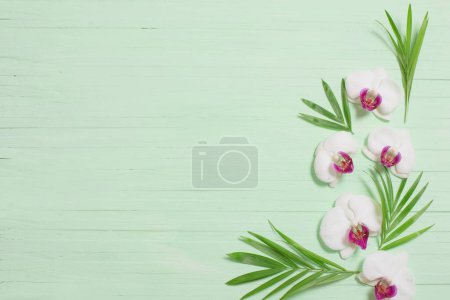 Foto de Flores de orquídea y hojas exóticas sobre fondo de madera verde - Imagen libre de derechos
