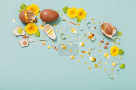 Téléchargez les photos : Oeuf au chocolat de Pâques avec confettis dorés et fleurs de printemps sur fond de papier menthe bleue - en image libre de droit