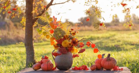 Foto de Ramo de flores de otoño en jarra rústica sobre mesa de madera al aire libre al atardecer - Imagen libre de derechos