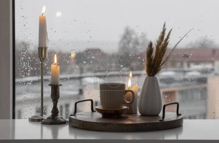 Foto de Naturaleza muerta de otoño con velas encendidas y una taza de café en el fondo de una ventana con gotas de lluvia - Imagen libre de derechos