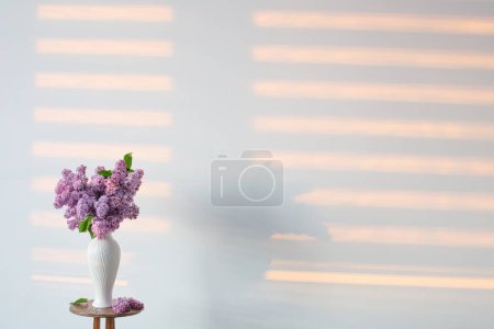 Foto de Flores lila en jarrón blanco sobre fondo pared blanca - Imagen libre de derechos
