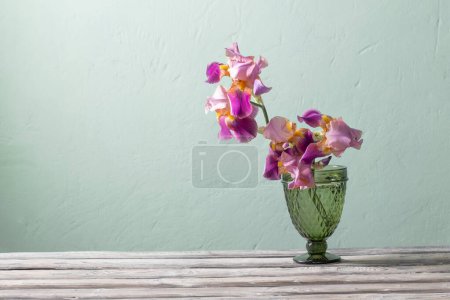 Téléchargez les photos : Iris dans un beau vase en verre contre le mur vert - en image libre de droit