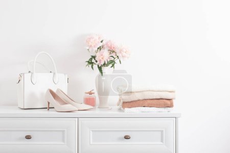 Photo for White dresser with clothes and flowers in white room - Royalty Free Image