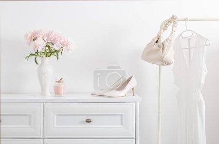 Photo for White dresser with clothes and flowers in white room - Royalty Free Image