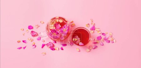 Téléchargez les photos : Thé avec pétales de rose dans une théière en verre sur fond rose - en image libre de droit