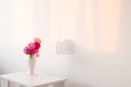 Téléchargez les photos : Roses roses dans un vase blanc sur la table sur fond blanc mur - en image libre de droit