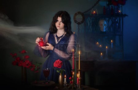 Foto de Joven hermosa mujer en vestido vintage azul con rosas rojas poción makind en habitación oscura - Imagen libre de derechos