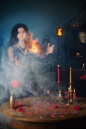 Téléchargez les photos : Jeune belle femme en robe vintage bleue avec des roses rouges et des potions magiques dans la chambre noire - en image libre de droit