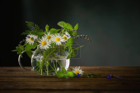 Foto de Ramo de flores de verano en tetera de vidrio sobre fondo oscuro, concepto de té de hierbas saludable - Imagen libre de derechos