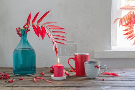 Téléchargez les photos : Feuilles d'automne rouges dans un vase en verre et baies de viorne et tasse de thé sur une table en bois - en image libre de droit
