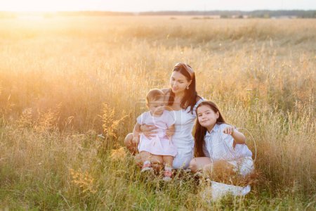 Foto de Feliz mamá con dos hijas pequeñas en el campo de verano al atardecer - Imagen libre de derechos