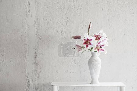 Téléchargez les photos : Beaux lis dans un vase en céramique sur fond blanc mur - en image libre de droit
