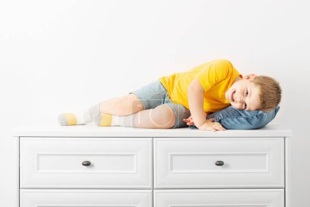Foto de Divertido chico acostado en la cómoda sobre fondo blanco - Imagen libre de derechos