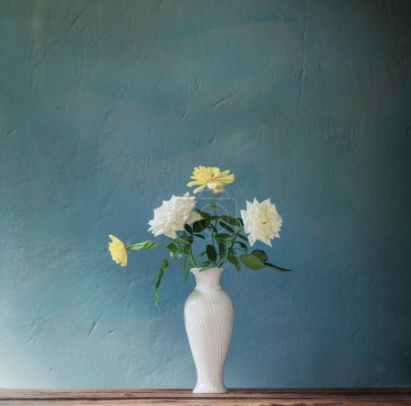 Foto de Rosas en jarrón blanco sobre mesa de madera sobre fondo pared oscura - Imagen libre de derechos