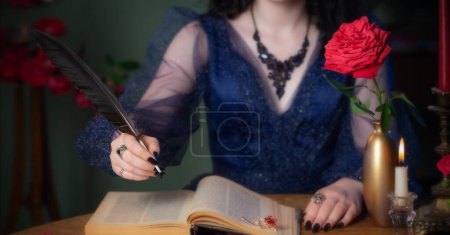 Téléchargez les photos : Jeune belle femme en robe vintage bleue avec livre sur table dans la chambre noire - en image libre de droit