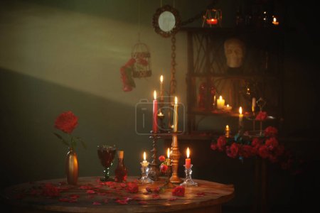 Téléchargez les photos : Potion magique aux roses rouges et aux bougies allumées dans la chambre noire - en image libre de droit