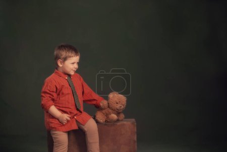 Téléchargez les photos : Petit garçon avec ours en peluche et vieille valise sur fond sombre - en image libre de droit