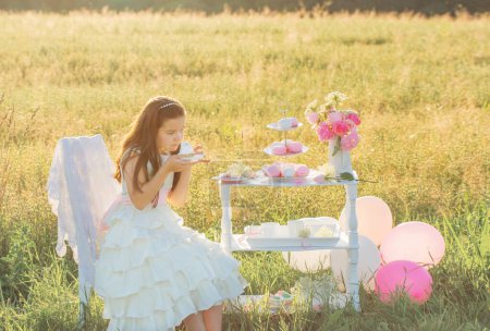Téléchargez les photos : Heureuse petite fille en robe blanche avec gâteau d'anniversaire dans le champ d'été - en image libre de droit