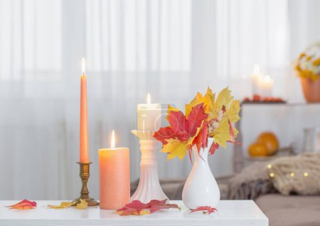 Photo for Burning candles with autumn decor on white table at home - Royalty Free Image